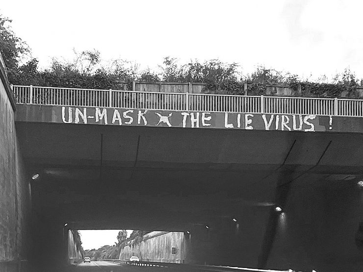 'Un-mask the lie virus' graffiti on a bridge parapet